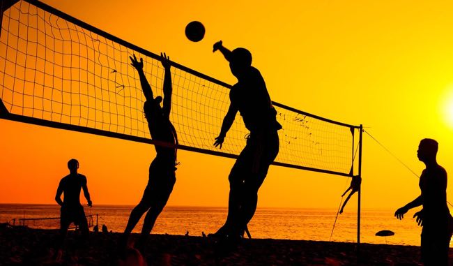 People playing beach volleyball on a sandy shore by the ocean.