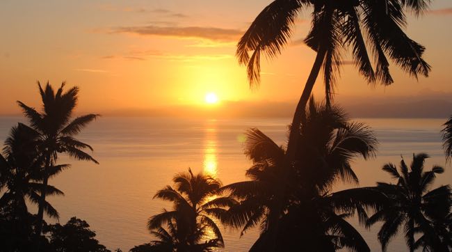 A vibrant Fiji sunset over the ocean, with colorful skies and silhouettes.
