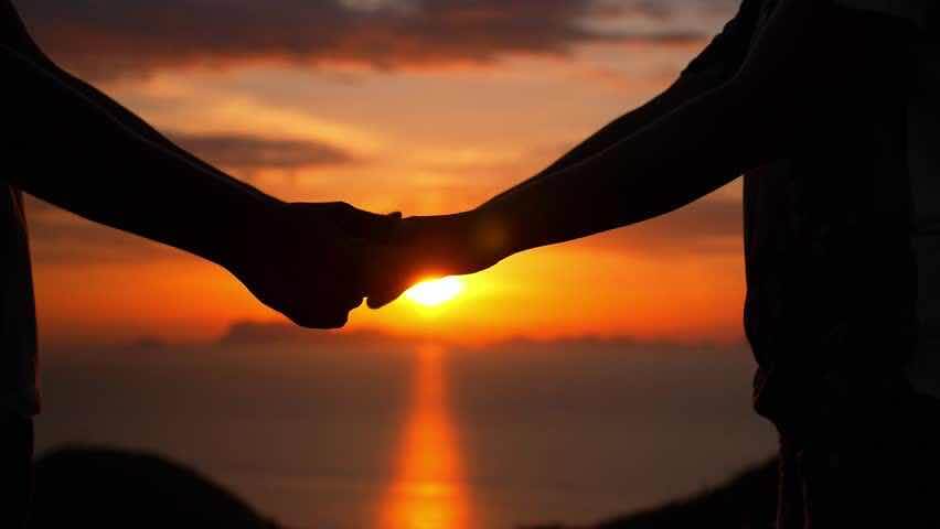 A couple holding hands during a sunset, with a golden sky.
