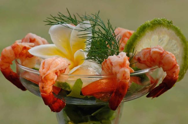 plump shrimp arranged around a glass with red cocktail sauce, garnished with lime
